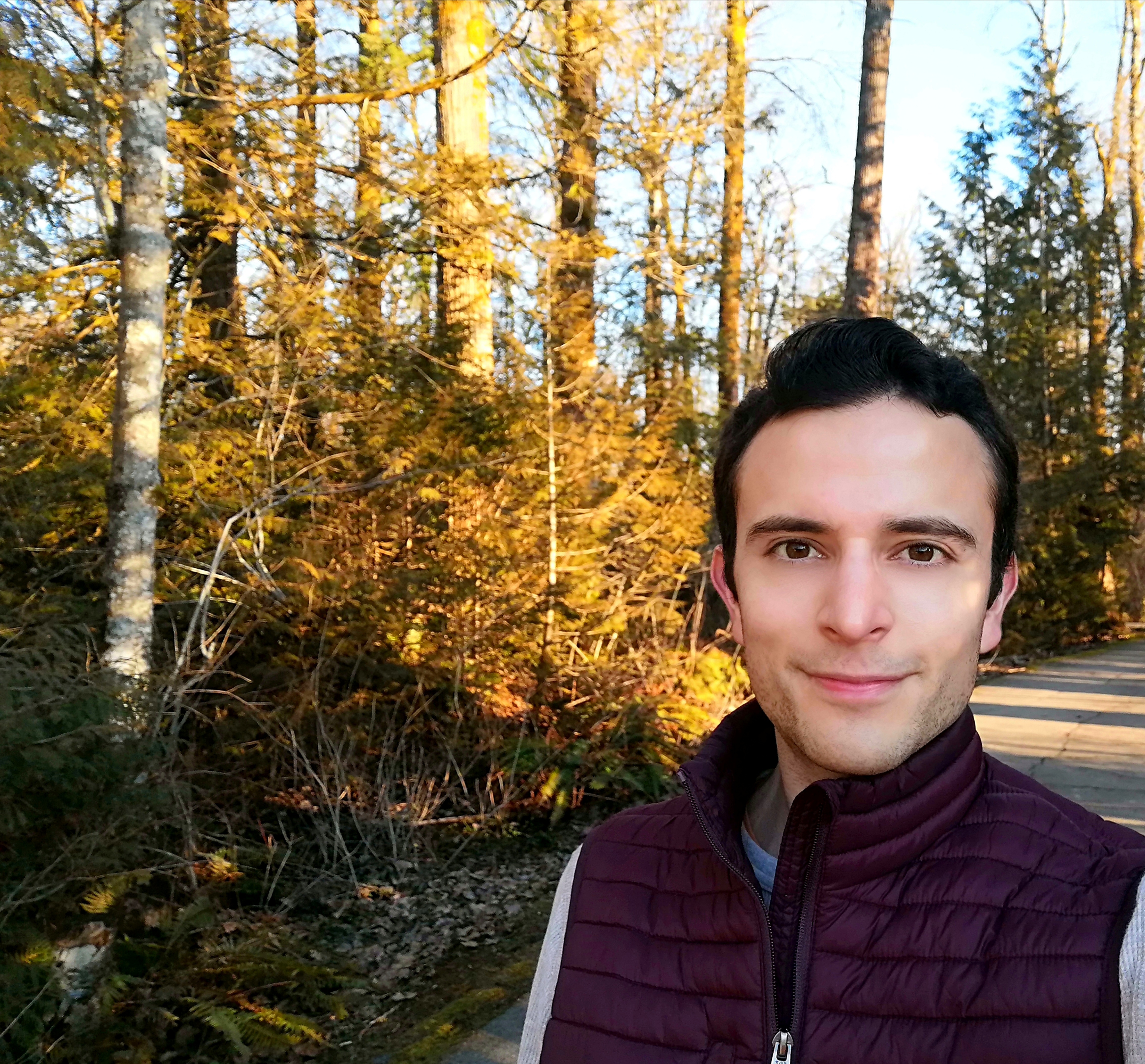 Student standing in a forest pathway wearing puffy vest in sunny afternoon weather.
