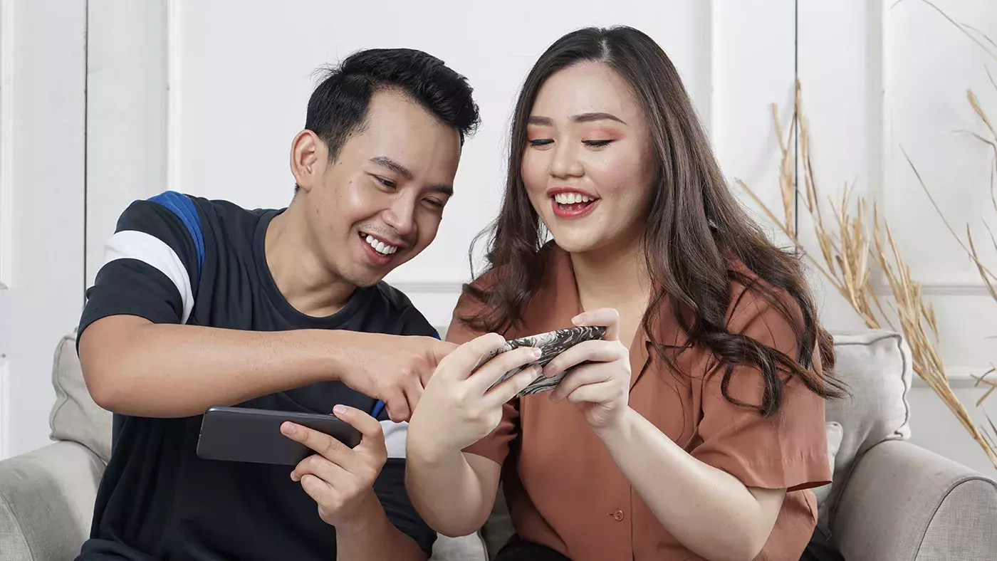 Two people smile while they gesture at a mobile device