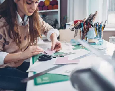 women with brown hair crafting with paper, ruler, and scissors  