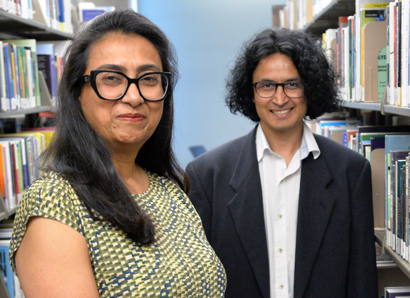 Dr. Asma Sayed and Dr. Pushparaj Acharya stand in a library aisle.
