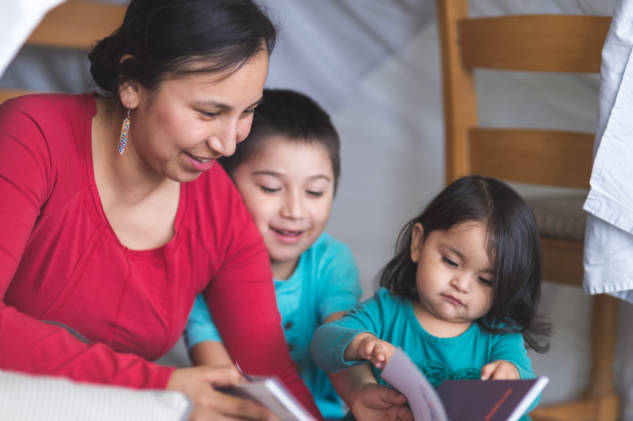 An Indigenous mother reads with her children in a makeshift living room fort.