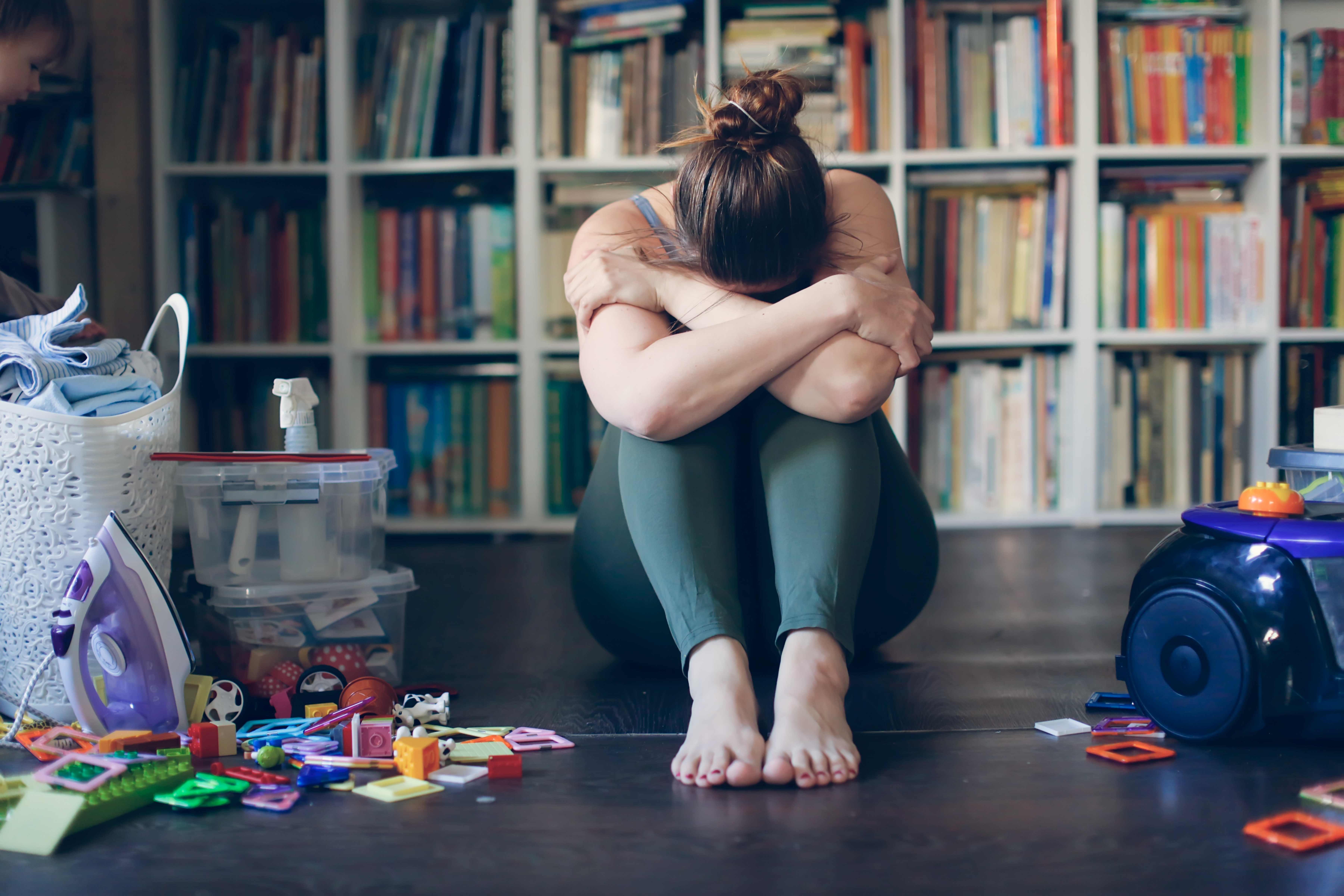 Overwhelmed woman in hunched position with vacuum cleaner and laundry basket.