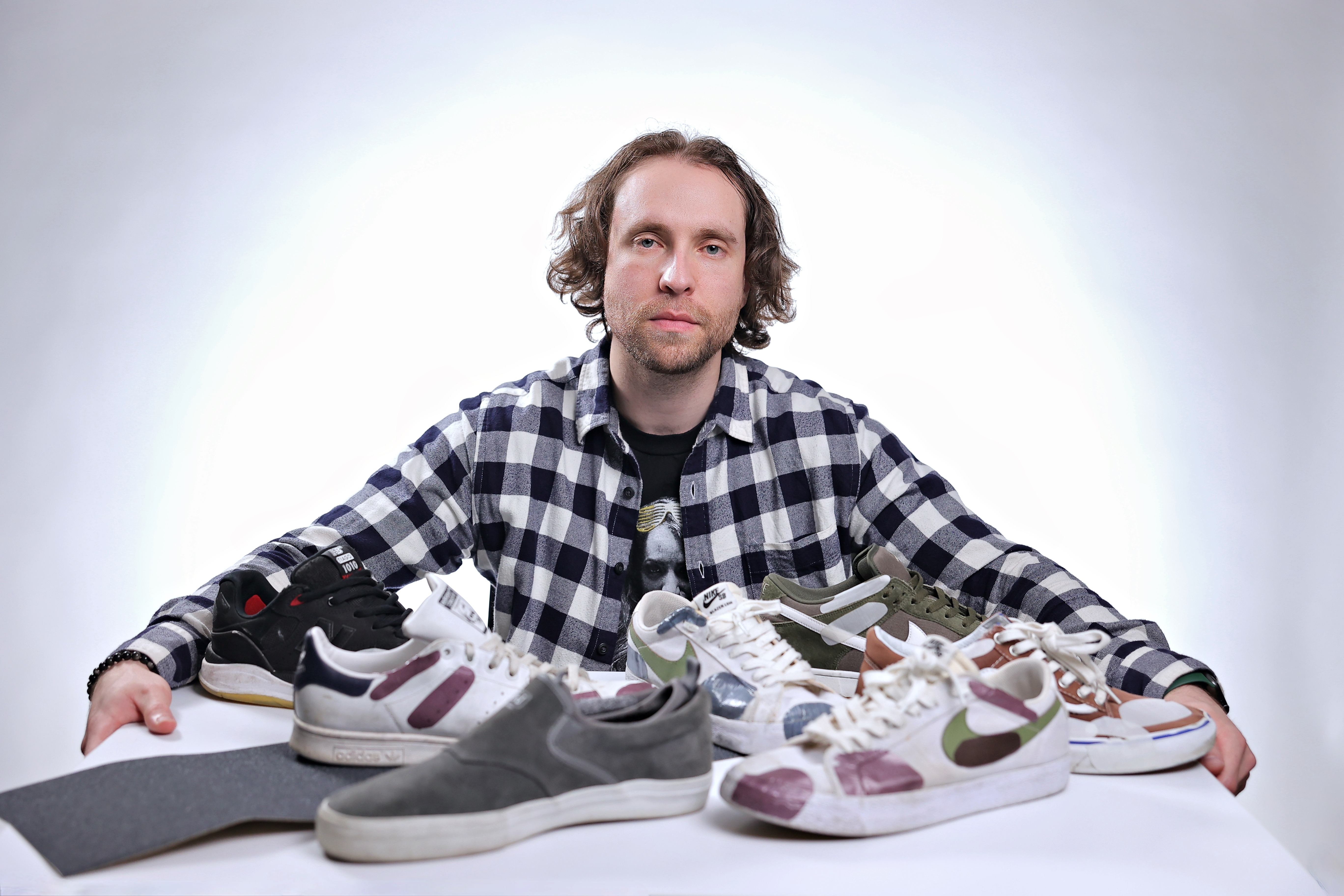 man wearing plaid shirt sitting at a table with several skateboarding shoes