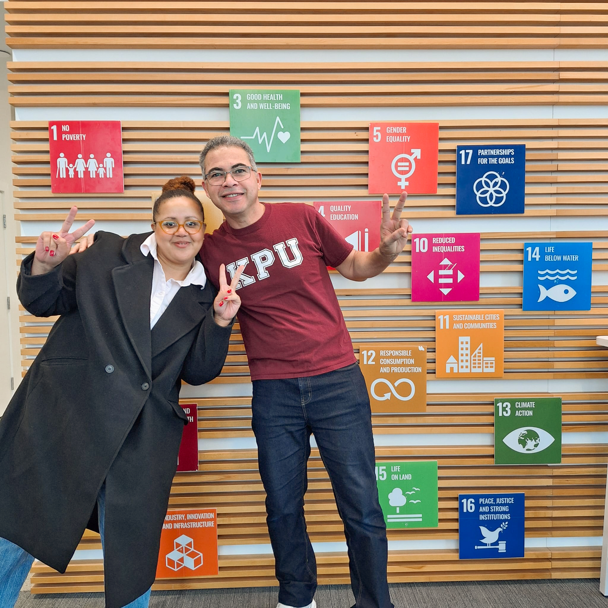 two people holding the peace sign infront of a wall with colourful squares