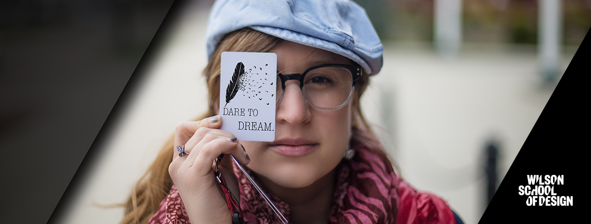 Student with business card covering one eye.