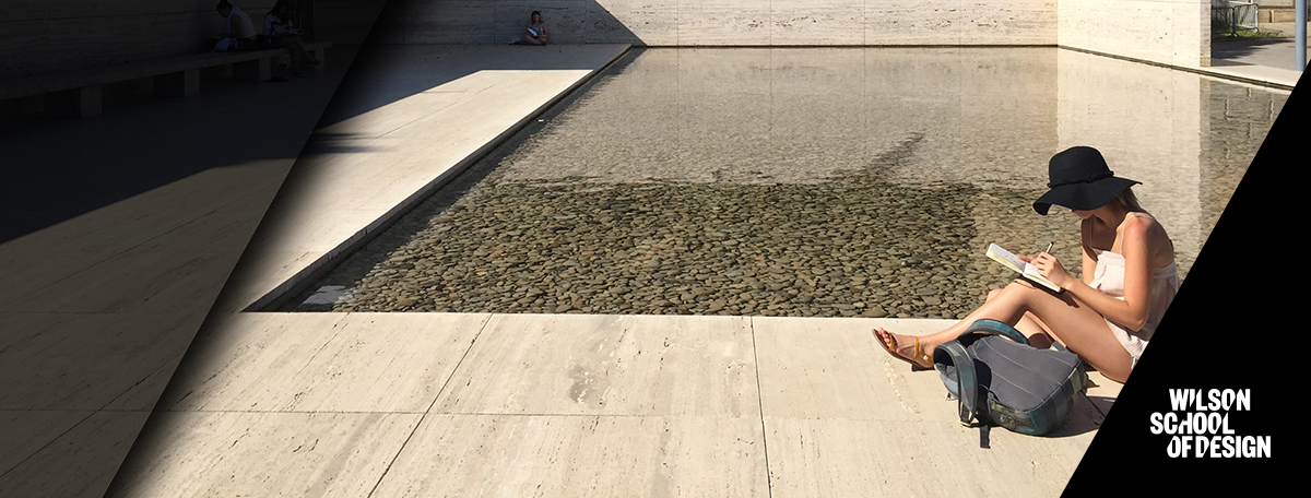 Student sitting by fountain doing homework.