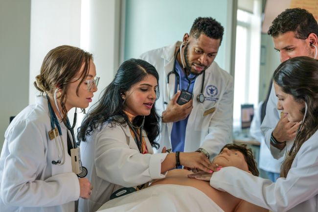 Medical students gather around a medical simulation dummy.