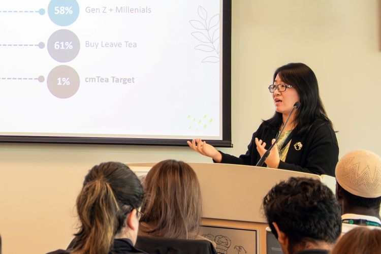 KPU student Chunmei Liu speaks at a podium in front of a small crowd.