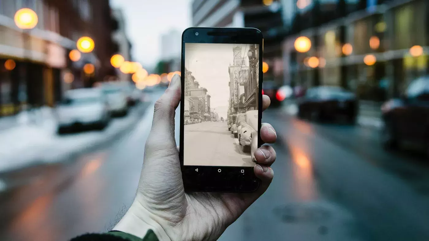 A photograph of a mobile phone captures the past and present appearance of a street