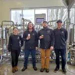 Mike Patterson (centre left) holding a can of beer and Michael Hodgson (centre right) holding a glass of beer with KPU brewing instructors Emily Kokonas (left) and Jon Howe (right), standing in front of brewing equipment